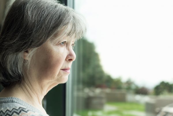 Older woman feeling lonely whilst starting out the window